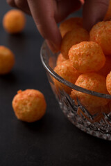Hand taking a cheese snack from a glass pot with cheese sticks and cheese balls on a black wooden table 