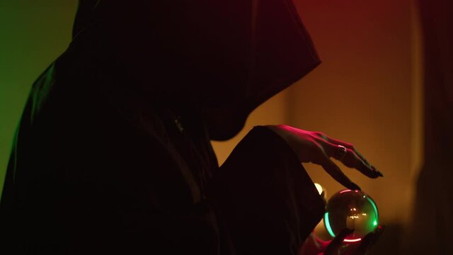 Witch woman holding magic crystal ball close-up. Fortune teller performing ritual, magician making rite or sacrifice using witchcraft. Halloween theme, sorceress wearing black gown robe.