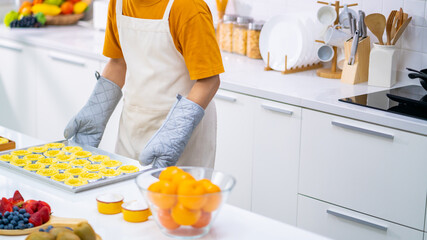 Asian man bakery shop owner preparing bakery in the kitchen. Male baker baking tart dough for making fruit tart on the table. Small business entrepreneur and indoor activity lifestyle concept.