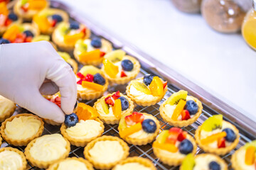 Asian man bakery shop owner preparing bakery in the kitchen. Male pastry chef making fruit tart with cream cheese on kitchen counter. Small business entrepreneur and indoor activity lifestyle concept.