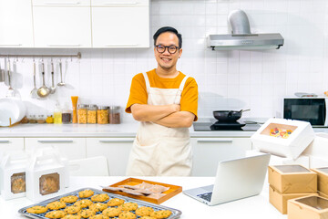 Portrait of Asian man bakery shop owner using laptop computer advertising online bakery store on social media in the kitchen. Small business entrepreneur and online marketing food delivery concept