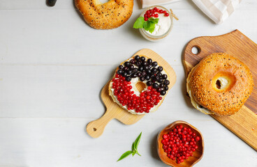 Open bagel with cream cheese, fresh cranberries and blueberries, on a wooden board. Overhead, copy of the space, horizontal