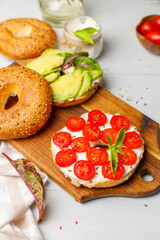 Open bagel sandwich with cream cheese, sweet tomatoes and avocado. Close-up on a light gray background, vertical