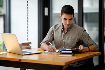 Young handsome man or businessman working on laptop computer in modern office.doing finances,accounting analysis,report,data and pointing graph Freelance education and technology concept.