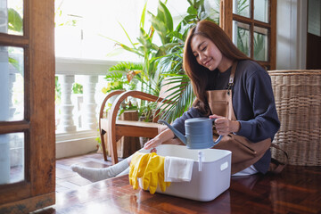 A young woman picking watering can up from a cleaning tools bucket at home © Farknot Architect