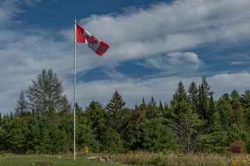 Canadian Flag on a pole with beautiful blue and cloudy sky in a rural environment