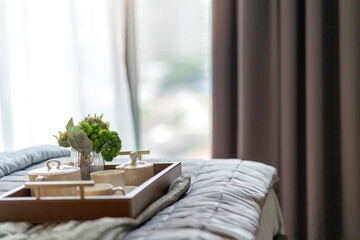 close up wooden tea tray and glass flower vase decoration on soft white bed at bedroom with soft sun light morning weekend vacation