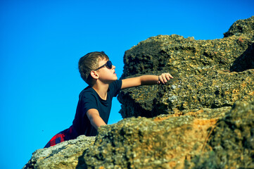 A little boy climbs a rock . Children's extreme entertainment