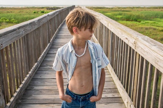 Male child with open shirt walking leisurely on beach boardwalk 