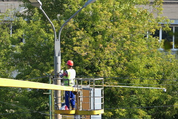 Street lamps on poles. A man in special clothes and a helmet on his head repairs a street lamp on a pole.