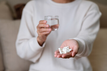 A woman holding white pills and a glass of water