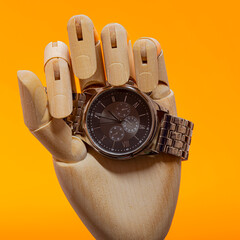 Wooden Hand with moden chronograph watch on an orange background
