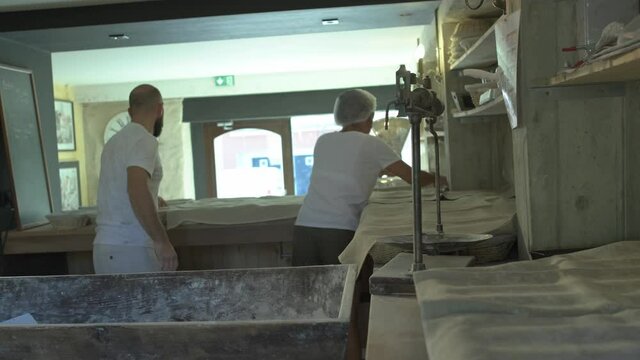 mid shot of two bakers preparing traditional french bread, kneading dough, placing it in osier basket, and covering with linen blanket