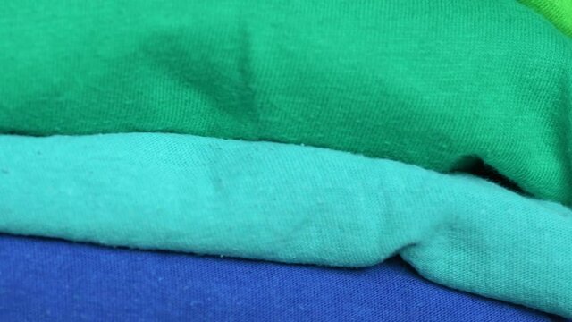 A stack of folded fabrics of different colors, sorted by shade. T-shirts stacked neatly on top of each other.