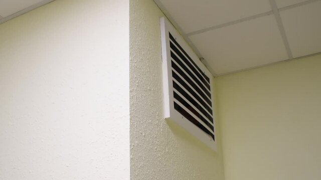 Ventilation grill on a white wall mounted under the ceiling. View of the ventilation hole inside the building.