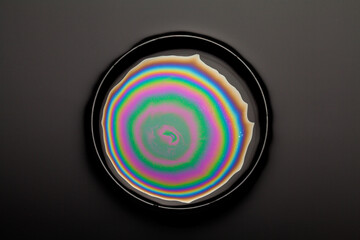 iridescent oil in dish on black background.