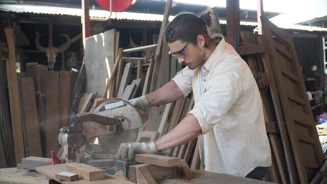 carpenter using circular saw cutting wooden plank in workshop . Young man builder sawing board . craftsman wearing protective safety glasses .