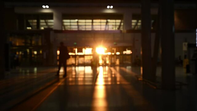 (Defocused video) Blurred silhouette of some tourists walking inside an airport terminal during a stunning sunset. Travel concept during the Covid-19 pandemic.