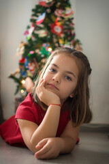 Portrait Of A Girl Lying On The Floor Next To The Christmas Tree, She Is Inside The House And She Is Looking At The Camera.