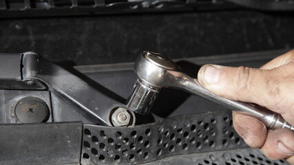 Service man hand with wrench tool unscrews the wipers drive arm closeup under hood, vehicle repair