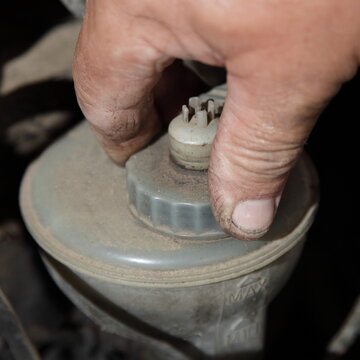Rapair man hand unscrews the power steering fluid tank, PSF level check under hood of the old car - vehicle maintenance service