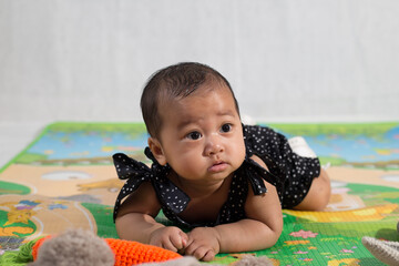 6-12 months old asian baby girl clothed in black crawling on the mat on the floor. Baby looking away with curiosity. 