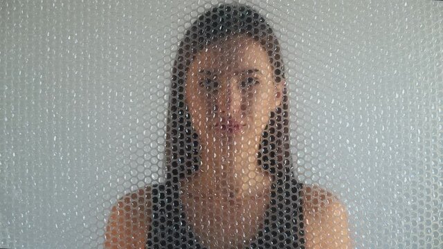 Woman freedom. Social isolation. Female rights. Single loneliness. Defocused slave silhouette trapped behind transparent bubble wrap on light out of focus background.