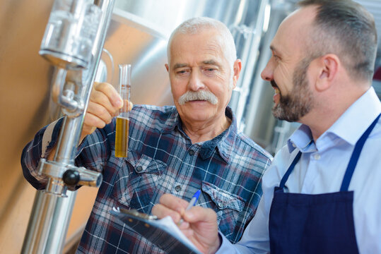 two manufacturer examining beer in test tube at brewery