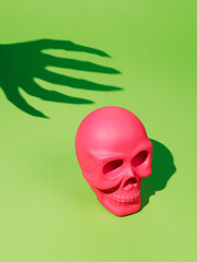 Pink human skull with a spooky hand shadow catching it from behind on a neon green background. Creative Halloween party concept. Pop art invitation card visual trend.