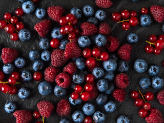  Raspberries, red currants and blueberries on a dark plate in a low key. Close-up. View from above. flat lay.