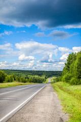 Fototapeta na wymiar Straight road with a marking on the nature background. Open Road in future, no cars, auto on asphalt road through green forest, trees. Clouds on blue sky in summer, sunshine, sunny day. Bottom view