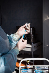 the hands of the nurse hold the syringe and ampoule. dark background. close-up. vertical frame.