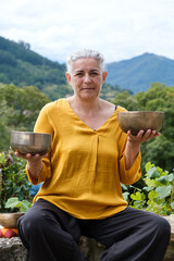 Portrait of mindful woman holding two singing bowls on her hands. Vertical photo.