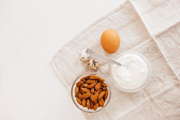 Nuts almonds, sour cream or yogurt, chicken and quail eggs on a linen kitchen towel on a white table. Healthy food and nutrients for proper nutrition of the brain and body concept