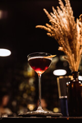 A classic Manhattan cocktail garnished with an orange zest in a beautiful glass at the bar