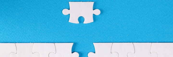 Unfinished white puzzle lying near last piece on blue background closeup