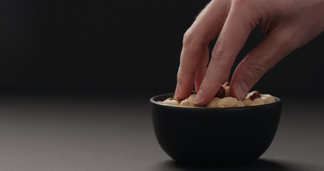 man hand take roasted hazelnuts from black bowl on black background