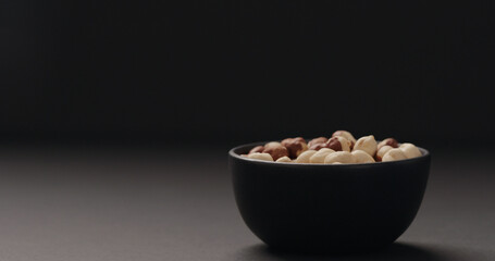 roasted hazelnuts in black bowl on black background