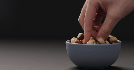 man hand take roasted hazelnuts from blue bowl on black background