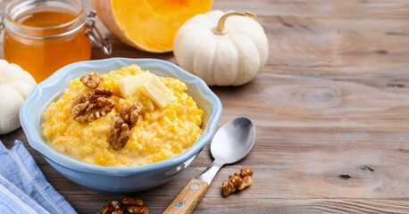Pumpkin rice milk porridge with walnuts, butter and honey in a blue bowl on a wooden table. Healthy food. Copy space. Selective focus 