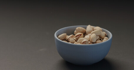 salted pistachios in blue bowl on black background