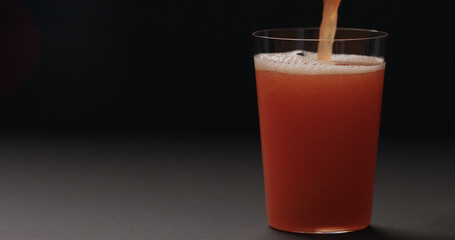 pour grapefruit juice in tumbler glass on black background
