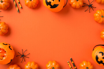 Top view photo of halloween decorations pumpkin baskets with candy corn spiders and straws on isolated orange background with copyspace in the middle