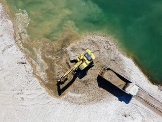 Excavator digging and loading sand into dump truck at river bank. Heavy machinery working at sand...