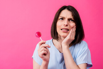 Young woman with sensitive teeth eating sweet lollipop on color background