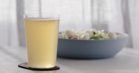 closeup ginger beer in a tumbler glass on oak table with blue bowl on background