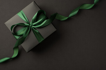 Top view photo of stylish black giftbox with green satin ribbon bow on isolated black background with empty space