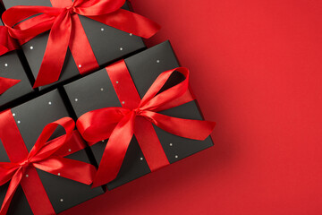 Top view photo of gift boxes in black packaging with sequins and red ribbon bow on isolated red background with copyspace