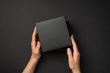 First person top view photo of hands holding open lid on black giftbox on isolated black background...