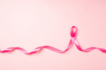 Top view photo of curly pink satin ribbon symbol of breast cancer awareness on isolated pastel pink...